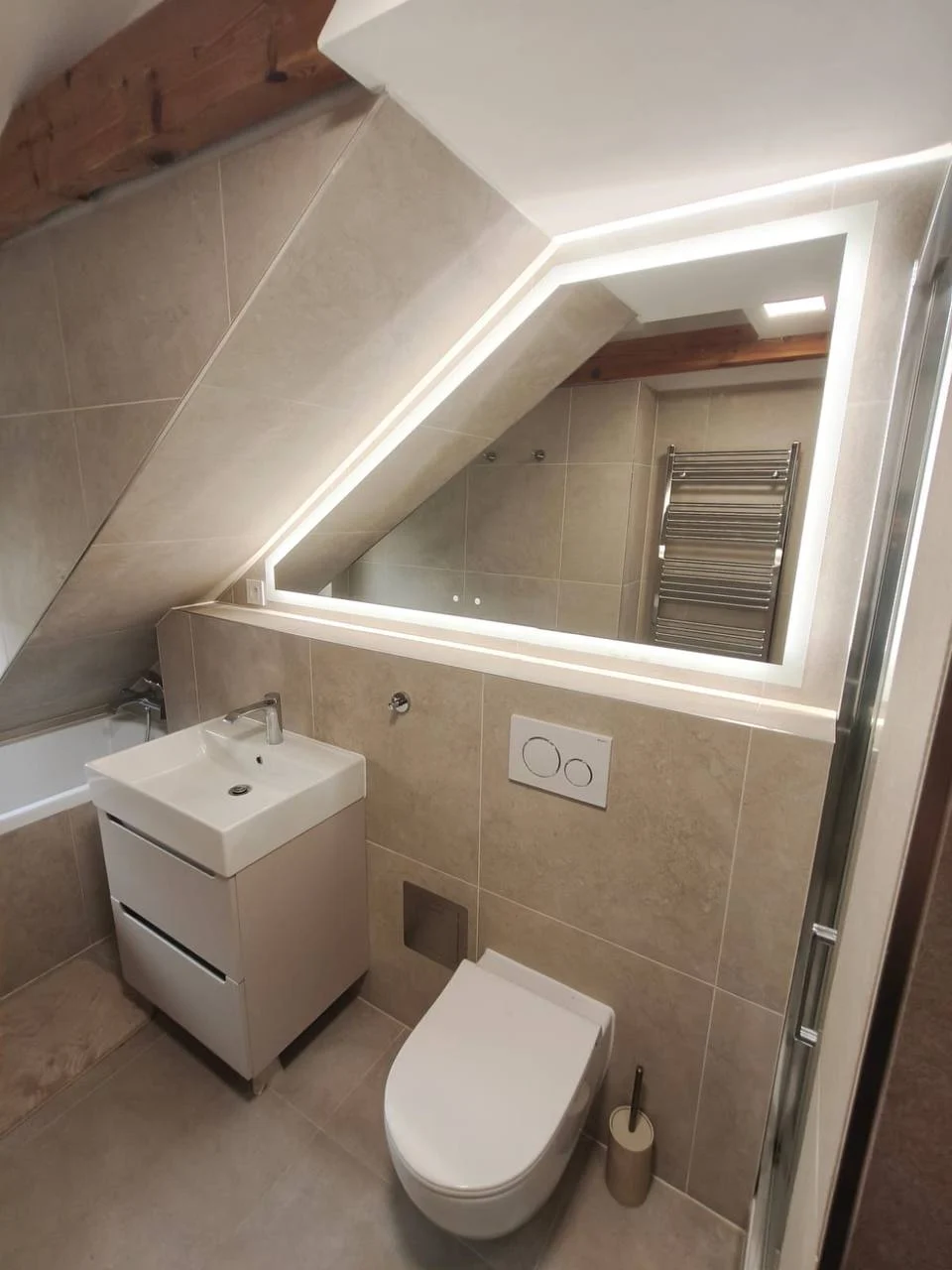 Umyvadlo a závěsné WC pod osvětleným zrcadlem v podkrovní koupelně